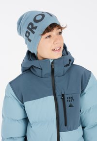 Blaue und graue Steppjacke mit Kapuze, ausgestattet mit einer Reißverschlusstasche und Logo-Detail. Die passende Strickmütze hat auffällige schwarze Buchstaben.