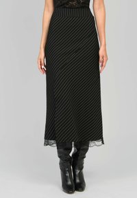 Jupe noire midi avec des rayures blanches diagonales, bord en dentelle à l'ourlet, et une taille ajustée. Portée avec des bottes noires à hauteur de genou.