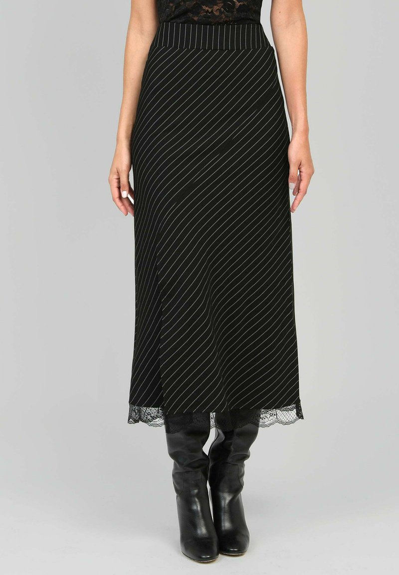 Jupe noire midi avec des rayures blanches diagonales, bord en dentelle à l'ourlet, et une taille ajustée. Portée avec des bottes noires à hauteur de genou.