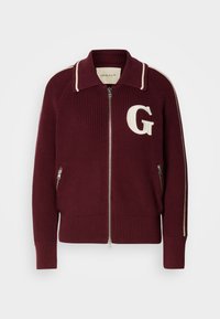 Maglione lavorato a maglia color bordeaux con zip, strisce bianche sul collo e sulle maniche, tasche con zip davanti e grande "G" bianca sul lato sinistro del petto.