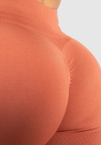 Perzikkleurige sportkledingstof met een rekbare, ribbelstructuur. Het ontwerp bevat een hoge halslijn en contournaad voor een betere pasvorm.