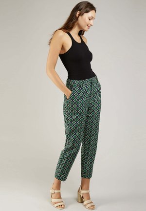 Pantalons à motifs multicolores avec des motifs géométriques verts, bleus et blancs, dotés de poches latérales et d'une coupe décontractée, associés à un débardeur noir.