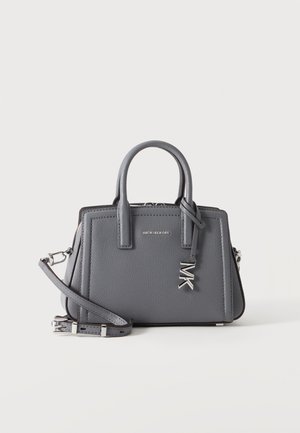 Grå Michael Kors håndtaske med top-håndtag, aftagelig skulderrem og sølv MK-vedhæng foran mod en ens hvid baggrund.