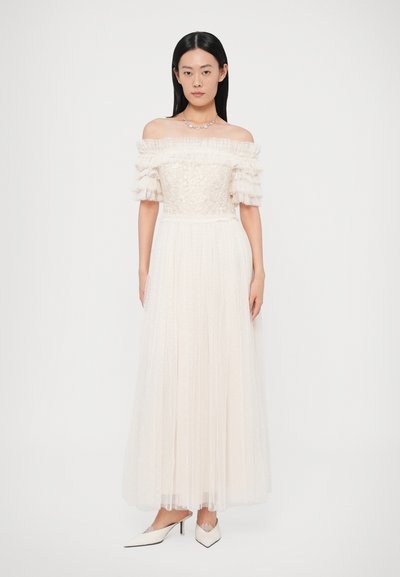Kremowa suknia z dekoltem odsłaniającym ramiona, plisowana spódnica z tiulu i kwiatowa haftowana górna część. Połączona z białymi, spiczastymi butami.
