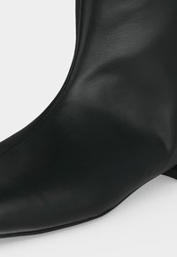 Bottine en cuir noir avec un bout pointu et un petit talon bloc, présentée sur fond blanc.