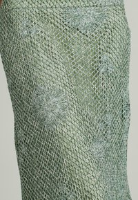 Mesh rok in lichtgroen, met uitgebreide bloemenborduursels. Getextureerd patroon met een glanzende afwerking en een vormgevende pasvorm.