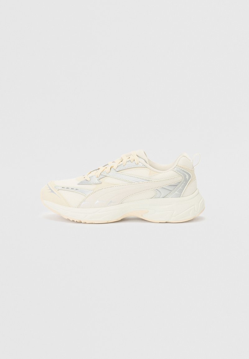 Chaussures de sport beige avec une tige en mesh et synthétique, une semelle incurvée et des accents réfléchissants. Elles présentent un design à lacets et une languette de traction à l'arrière.