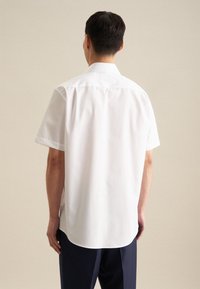 Camicia bianca a maniche corte con colletto classico, superficie liscia e orlo dritto, con yoke posteriore e design minimalista.