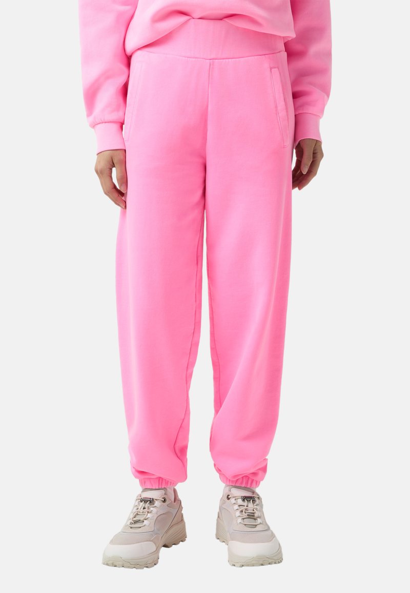 Rosa Sweatpants mit lockerer Passform, schmal zulaufenden Bündchen und Seitentaschen, aus weichem Stoff. Kombiniert mit beigen Sneakers für einen Kontrast.