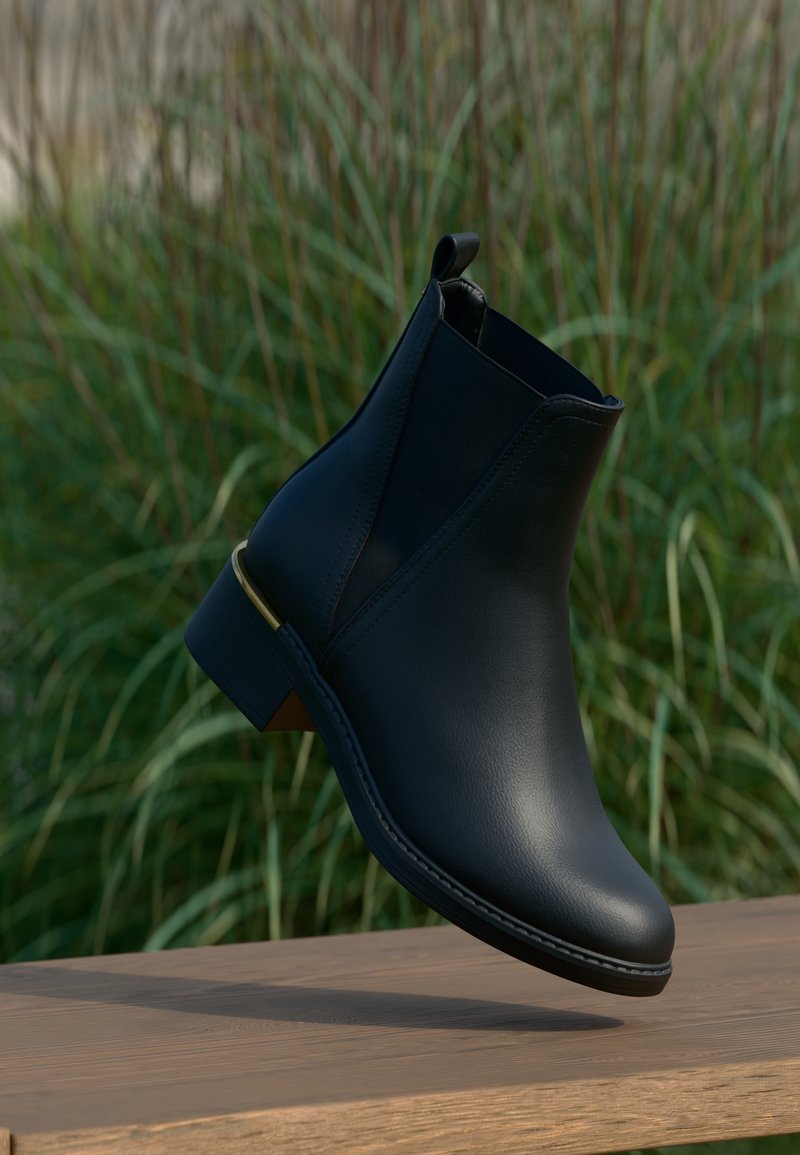 Bottine en cuir noir avec talon bas et languette de tirage, suspendue au-dessus d'une surface en bois avec un arrière-plan d'herbe verte.