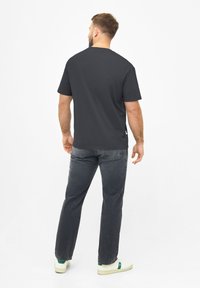 Donkergrijze katoenen T-shirt met korte mouwen, ronde hals en een subtiele logodetail aan de zoom, gecombineerd met donkere spijkerbroek en witte sneakers.
