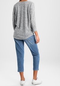 Maglione grigio a maglia morbida con scollatura rotonda e maniche a tre quarti, abbinato a jeans blu a sigaretta e sneakers bianche.