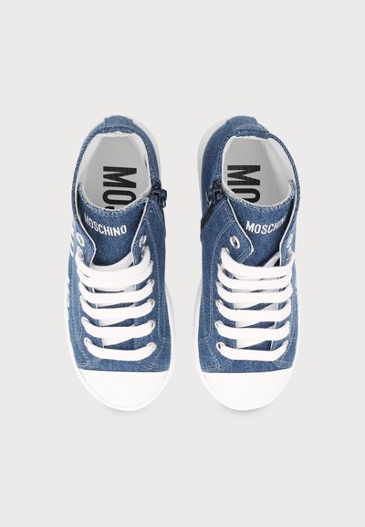 Ζευγάρι μπλε τζιν sneakers με λευκά κορδόνια και λαστιχένιες μύτες, με το λογότυπο Moschino στη γλώσσα και στην εσωτερική σόλα, φαίνεται από πάνω.