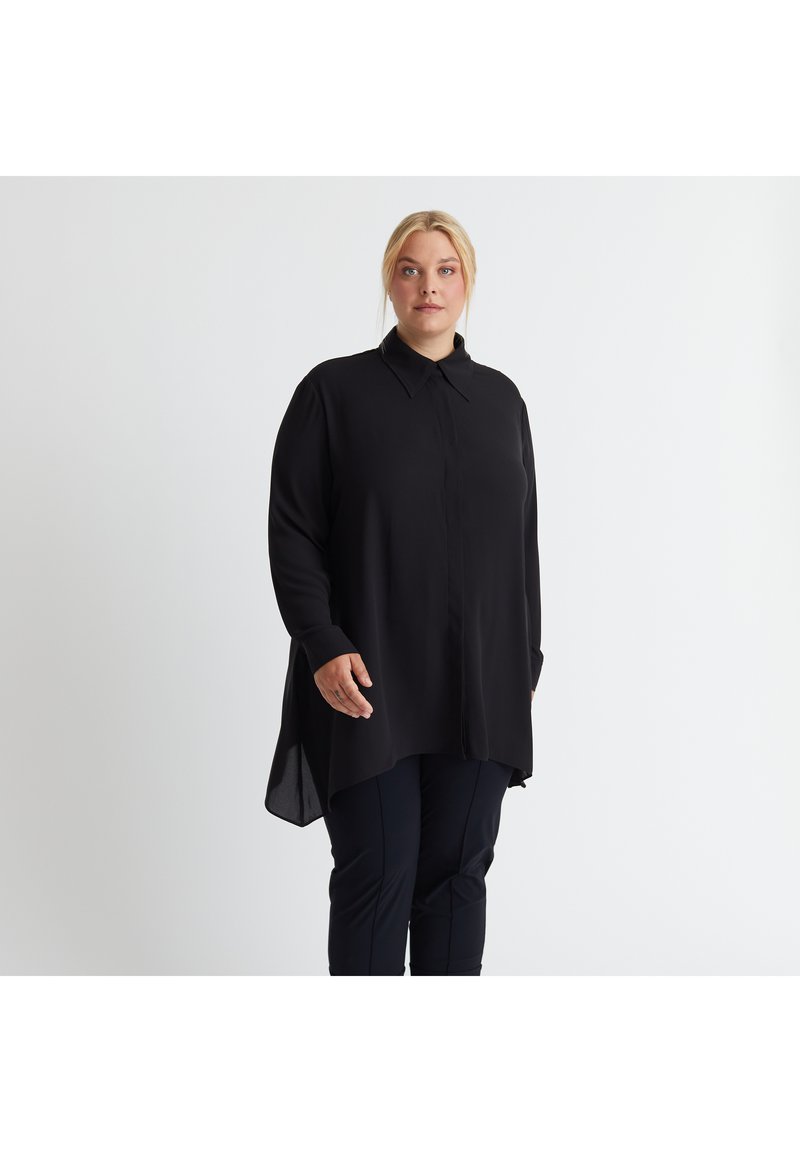 Schwarze Bluse mit langen Ärmeln, Kragen, durchgehender Knopfleiste, abgerundetem Saum und lockerer Passform, aus glattem Stoff gefertigt. Kombiniert mit dunklen Hosen.
