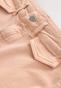 Jasnoróżowa bawełniana tkanina z delikatnym wzorem w paski, ozdobiona srebrnym guzikiem oraz przeszyciem kieszonki na pasie.