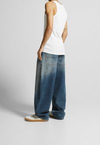 Vit ribbad linne i kombination med oversized bleka blå denimjeans. Vita sneakers med bruna sulor synliga nederst.