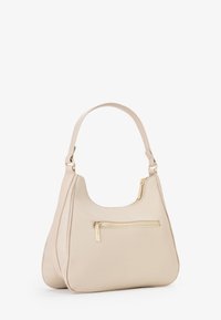 Borsa a spalla in finta pelle beige con forma arrotondata, tracolla singola e dettaglio della cerniera in tonalità oro sulla tasca frontale. Texture liscia, design minimalista.