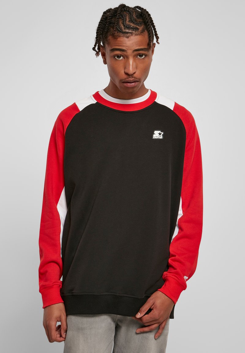 Felpa nera con maniche raglan rosse e bianche, colletto e polsini a costine, logo sul petto, tessuto misto cotone, vestibilità rilassata.