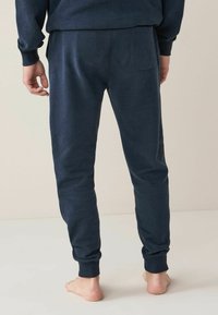Marinblå joggerbyxor i mjukt tyg med elastisk midjeband, muddar i bensluten och en enda bakficka.