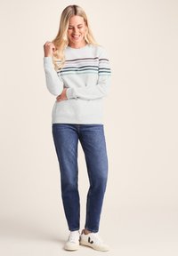 Light gray sweatshirt with horizontal multicolored stripes in shades of green, purple, and blue. Paired with dark blue jeans and white sneakers.