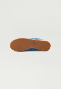 Tenis blue din suede cu un superior texturat, o talpă plată din cauciuc gumos cu un model circular pentru aderență și stabilitate.