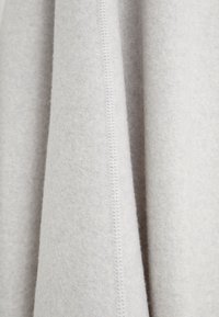 Jasnoszara wełniana tkanina wisi z miękką, szczotkowaną fakturą. Posiada proste przeszycia wzdłuż krawędzi, co podkreśla jej gładkie wykończenie.