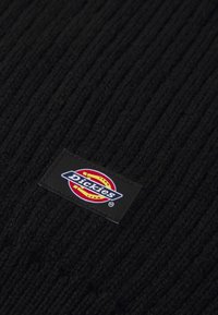 Sort ribbet hat lavet af tekstureret stof, med et rektangulært sort label med det farverige "Dickies" logo syet på den ene side.