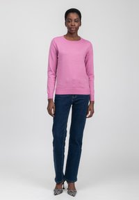 Maglione rosa a maglia con maniche lunghe e scollo rotondo, abbinato a jeans a gamba dritta blu scuro e scarpe con tacco alto a fantasia.