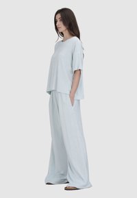 Lichtblauwe tweedelige outfit met een loszittende top met korte mouwen en wijde broek, gemaakt van zacht materiaal met zijzakken.