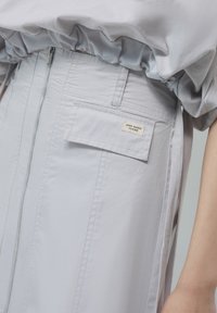 Gonna grigia chiara con zip frontale e tasca a pattina etichettata "Zero Waste Design" indossata con un top abbinato infilato dentro.