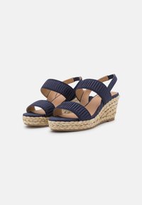 Marineblå kilehæle med to brede stropper, plisseret tekstur og en vævet jute-base. Åben tå-design med en polstret indersål.