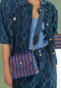 Gestreepte handtas met een combinatie van blauwe en bruine leer, voorzien van een magneetsluiting en een gestructureerde schouderband. Draagt met patroon denim.