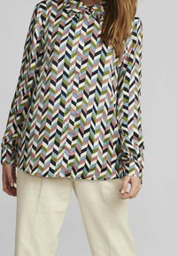 Chemise à manches longues présentant un motif chevron multicolore en rose, vert, bleu et marine, avec un col arrondi et une fermeture à boutons.