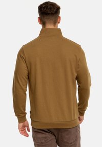 Brun pullover med høj krave, lange �ærmer og ribbede manchetter. Blødt stof med en glat tekstur, der har en subtil logodetail på siden.