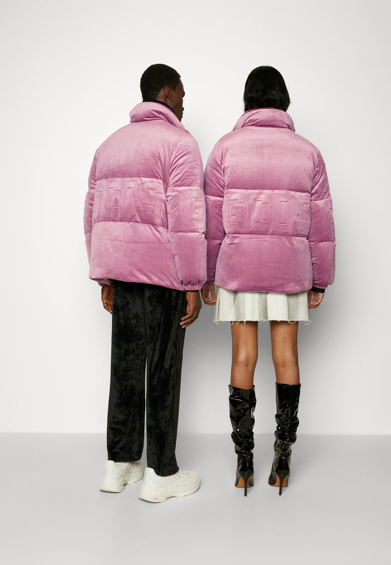 Giubbotti puffer in velluto rosa con logo "GCDS" in rilievo, vestibilità oversize, abbinati a pantaloni neri e stivali lucidi al ginocchio.