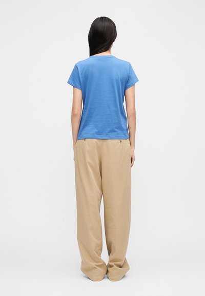 Kék rövid ujjú, puha pamutból készült póló laza bézs nadrággal párosítva. Mindkét ruhadarab laza, kényelmes szabású és egyszerű kialakítású.
