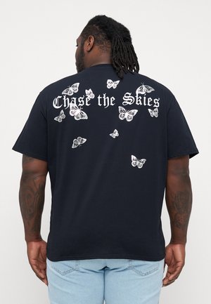 Schwarzes Baumwoll-T-Shirt mit weißen Schmetterlingsdrucken, die über den Rücken verteilt sind, und dem Text "Chase the Skies" über dem Design. Kurze Ärmel.