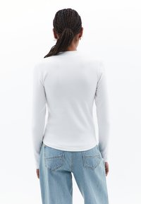 Weißes Langarmhemd mit Rundhalsausschnitt, taillierter Passform und glatter Textur, kombiniert mit hellblauen Jeans aus Denim mit Gesäßtaschen.