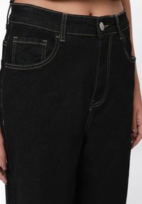 Sorte denimjeans med kontrastsømmer, en frontlomme og en metallknaplukking i livet. Rett passform.