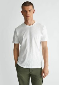 T-shirt bianco a maniche corte realizzato in tessuto leggero, con scollatura a girocollo e un leggero motivo testurizzato. Abbinato a pantaloni cargo verdi.