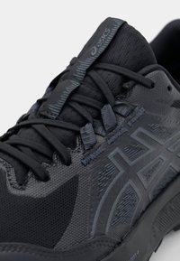 Black athletic shoe with a mesh upper, textured accents, and raised logo. Features flat laces and reinforced toe cap for support.
