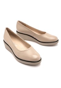 Beżowe buty na koturnie z gładką skórzaną cholewką, okrągłym noskiem, perforowaną wkładką i kontrastowym czarnym wykończeniem wzdłuż podeszwy.