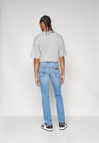 Camiseta de algodón gris con mangas cortas, combinada con jeans de mezclilla azul claro. Zapatillas negras y blancas con una textura suave y detalle de logo.