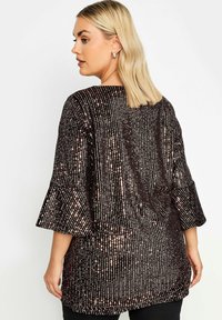 Top scuro con paillettes, dal taglio morbido, caratterizzato da ampie maniche a campana e motivi a righe verticali. Il dettaglio sul retro include un'accento con fiocco.