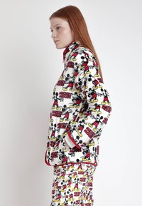 Set di pigiama in pile con un motivo di Topolino in rosso, giallo e nero su sfondo bianco; include una giacca con zip e pantaloni coordinati.