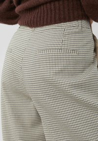 Pantalon à carreaux beige et bleu marine avec une coupe décontractée. Comprend deux poches arrière, un tissu texturé et des lignes épurées.