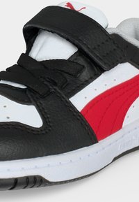 Μαύρο, λευκό και κόκκινο αθλητικό παπούτσι Puma με μαύρα κορδόνια και μαύρο λουράκι βέλκρο πάνω από τη γλώσσα, με το λογότυπο Puma σε κόκκινο.