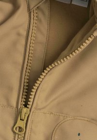 Un tissu beige à texture prononcée présente une fermeture éclair centrale, décorée de petites perles surélevées le long de la ligne de fermeture.