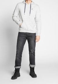 Grå huvtröja med dragsko och kenguruficka, i kombination med mörka jeans och svarta snörboots. Slätt tyg med ribbade muddar.