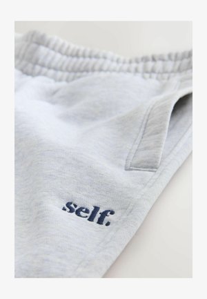 Pantalons de survêtement gris clair avec une taille élastique et une poche latérale, brodés du mot "self." en fil bleu foncé.